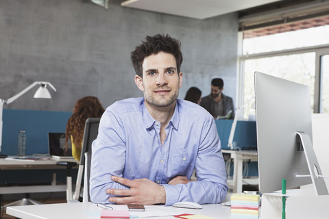 Porträt eines lächelnden Mannes an seinem Arbeitsplatz im Büro, lizenzfreies Stockfoto