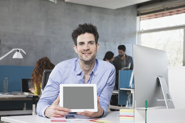 Porträt eines lächelnden Mannes, der einen Tablet-Computer im Büro zeigt - RBF001631