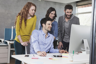 Vier Kollegen schauen auf einen Desktop-Computer im Büro - RBF001632