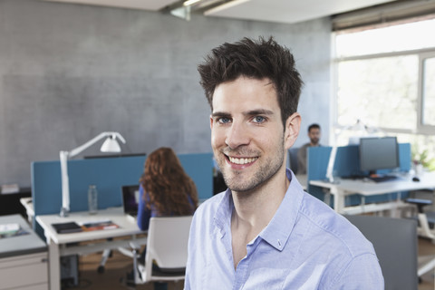 Porträt eines lächelnden Mannes, der in einem Großraumbüro sitzt, lizenzfreies Stockfoto