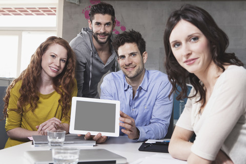 Gruppenbild von vier kreativen Menschen, die einen Tablet-Computer im Büro zeigen, lizenzfreies Stockfoto