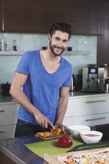 Porträt eines lächelnden Mannes beim Schneiden von Gemüse in seiner Küche - RBF001673