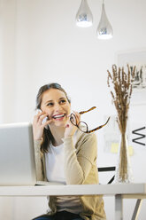 Porträt einer Frau, die in einem modernen Heimbüro mit einem Smartphone telefoniert - EBSF000171