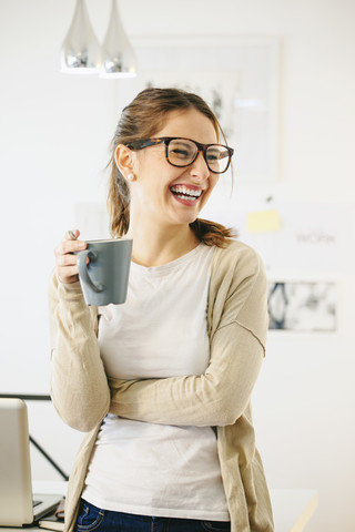 Porträt einer Frau mit Kaffeetasse in einem modernen Heimbüro, lizenzfreies Stockfoto