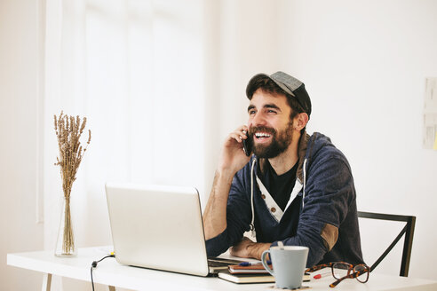 Portrait of man telephoning with smartphone at modern home office - EBSF000175