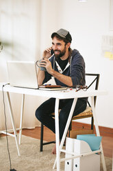 Porträt eines Mannes, der in einem modernen Heimbüro mit einem Smartphone telefoniert - EBSF000174