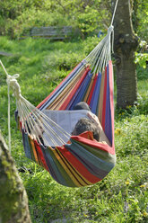 Germany, Young man lying in hammock and reading a magazine - LAF000722