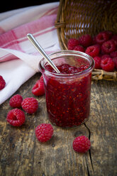 Glass of raspberry jam, kitchen towel and raspberries on wooden table - LVF001068
