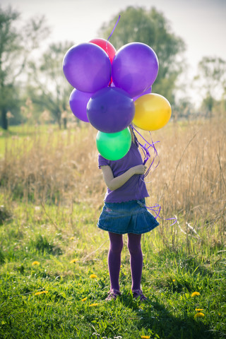Little girl's face hidden behind balloons stock photo