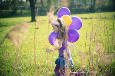 Kleines Mädchen mit Luftballons läuft auf einer Wiese - SARF000485