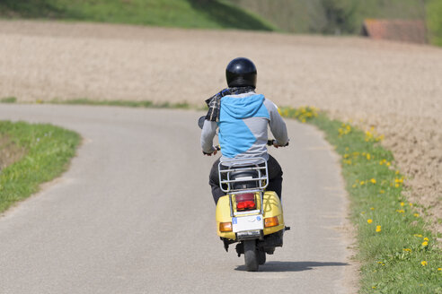 Junger Mann fährt mit seiner Vespa auf einer Landstraße - LAF000729