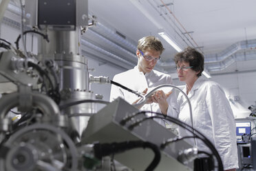 Zwei Wissenschaftler stehen in einem analytischen Labor mit einem Rasterelektronenmikroskop im Vordergrund - SGF000590