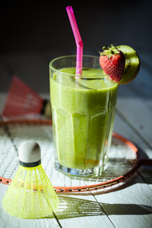 Glas mit garniertem Kiwi-Smoothie, Federbälle und Badmintonschläger auf Holztisch - SARF000503