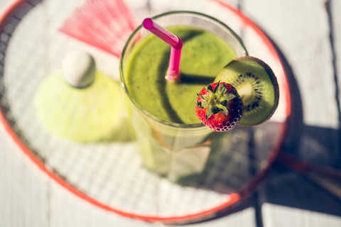 Glas mit garniertem Kiwi-Smoothie, Federbälle und Badmintonschläger auf Holztisch, lizenzfreies Stockfoto