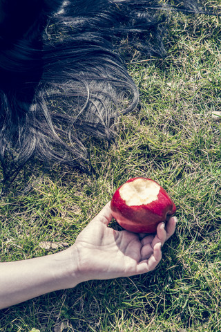 Hand einer im Gras liegenden Frau, die einen angebissenen roten Apfel hält, lizenzfreies Stockfoto