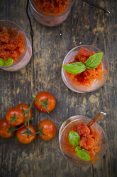 Glasses of tomato granita garnished with basil leaves and cherry tomatoes on dark wood, view from above - LVF001095