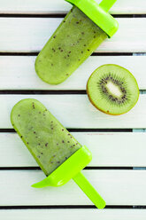 Two kiwi ice cream lollies and a half of kiwi on wood, view from above - LVF001104