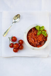 Marmorschale mit Tomatengranita garniert mit Basilikumblättern, Teelöffel und Kirschtomaten auf weißem Tuch, Ansicht von oben - LVF001107