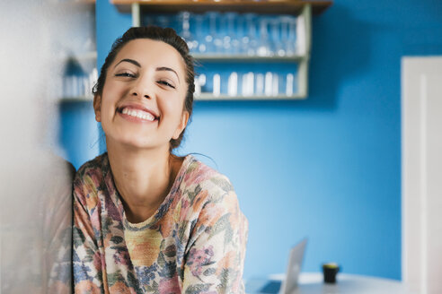 Porträt einer glücklichen jungen Frau, die sich in ihrer Küche an den Kühlschrank lehnt - MFF001023