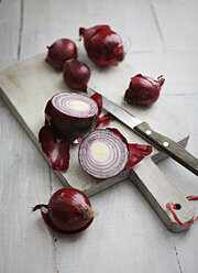 Rote Zwiebeln im Ganzen und in Scheiben geschnitten, Küchenmesser auf Holzbrett - KSWF001243