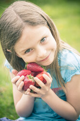 Porträt eines lächelnden kleinen Mädchens, das eine Handvoll Erdbeeren hält - SARF000519