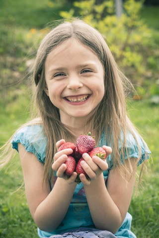 Porträt eines lächelnden kleinen Mädchens, das eine Handvoll Erdbeeren hält, lizenzfreies Stockfoto