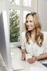 Blonde junge Frau am Schreibtisch mit einer Tasse Kaffee - MFF001065