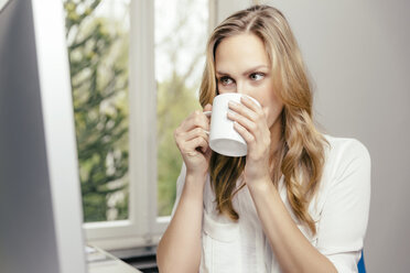 Blonde junge Frau am Schreibtisch trinkt eine Tasse Kaffee - MFF001064