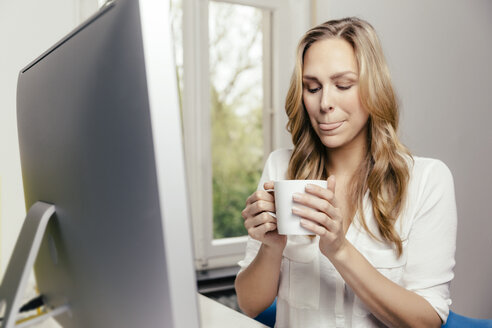 Blonde junge Frau am Schreibtisch trinkt eine Tasse Kaffee - MFF001063