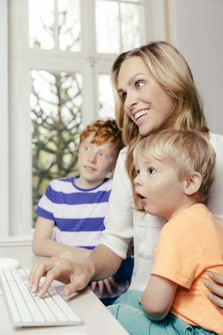 Glückliche Mutter mit zwei Söhnen, die auf einen Computerbildschirm schauen, lizenzfreies Stockfoto