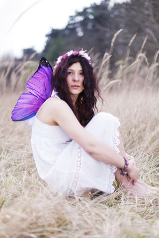 Germany, Young woman with wings sitting on meadow stock photo