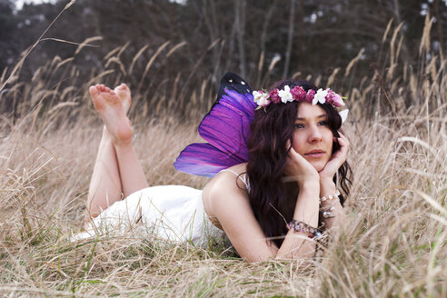 Germany, Young woman with wings lying on meadow - AFF000056