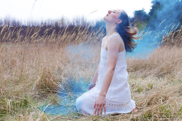 Germany, Young woman and blue powder of the Holi Festival sitting on meadow - AFF000057