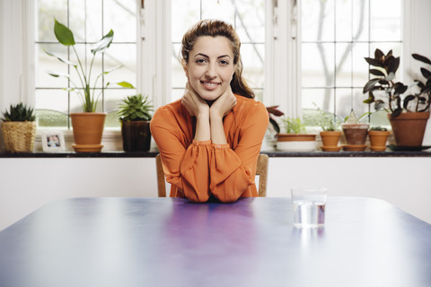 Porträt einer lächelnden jungen Frau, die zu Hause am blauen Tisch sitzt, lizenzfreies Stockfoto