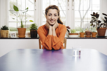 Portrait of smiling young woman sitting at blue table at home - MFF001048