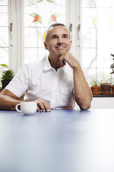 Porträt eines lächelnden Mannes mit einer Tasse Kaffee an einem blauen Tisch - MFF001044