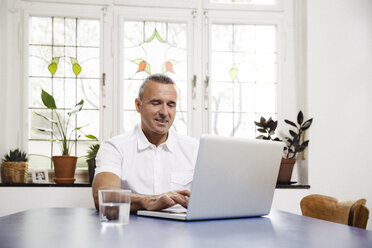 Porträt eines lächelnden Mannes, der zu Hause einen Laptop benutzt - MFF001054