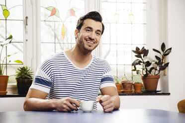 Portrait of happy young man sitting at blue table with a cup - MFF001043