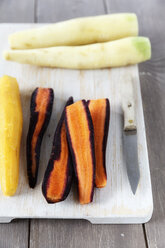 Different sorts of whole and sliced carrots, kitchen knife on chopping board and wooden table - EVGF000543