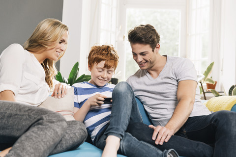 Junge Familie sitzt auf der Couch und schaut auf ihr Smartphone, lizenzfreies Stockfoto