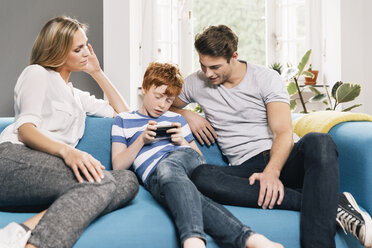 Young family sitting on couch looking at smartphone - MFF001082