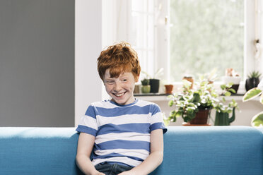 Junge sitzt auf blauer Couch im Wohnzimmer - MFF001079