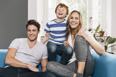 Portrait of laughing young family sitting on their couch at living room - MFF001074