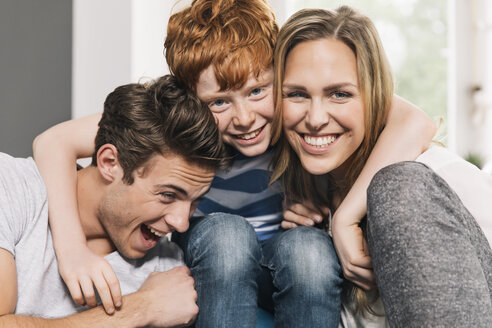 Porträt einer glücklichen jungen Familie, die auf ihrer Couch im Wohnzimmer sitzt - MFF001073