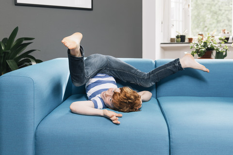 Junge, der sich auf der blauen Couch im Wohnzimmer herumwälzt, lizenzfreies Stockfoto