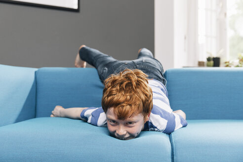 Boy rollicking around on blue couch in living room - MFF001071