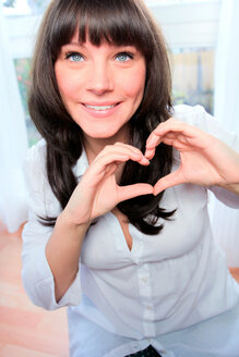 Portrait of smiling dark-haired woman forming heart with her hands - AFF000069