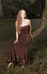 Junge Frau mit Abendkleid auf einem Baumstamm im nächtlichen Park sitzend - FCF000055