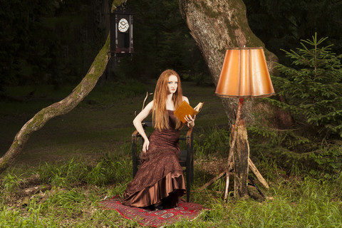 Junge Frau mit Abendkleid sitzt auf einem Stuhl im nächtlichen Park, lizenzfreies Stockfoto