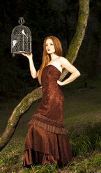 Young woman with evening dress holding birdcage in park by night - FCF000058